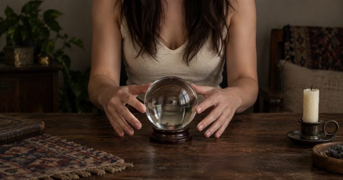 Reading table — repaired horizontal cover A woman in a cream top holds her hands beside a clear crystal ball on a home table.
