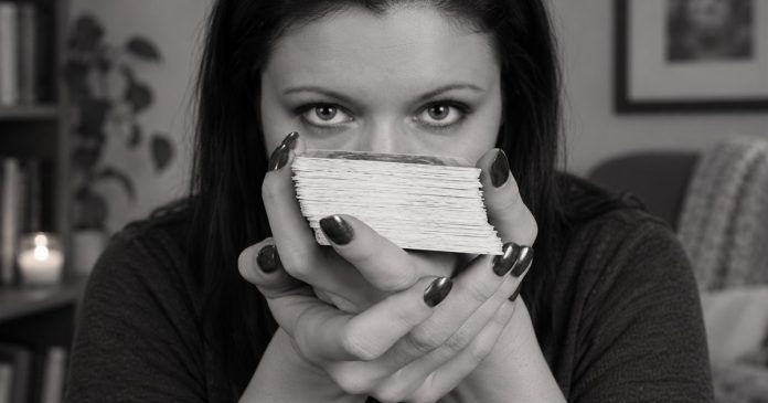 Black-and-white portrait of a woman holding a deck of cards in a modest home setting