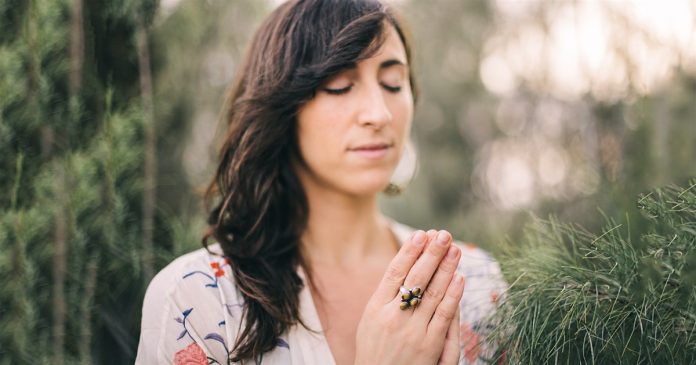 A quiet spiritual pause outdoors Woman with closed eyes and joined palms in a softly lit outdoor garden.