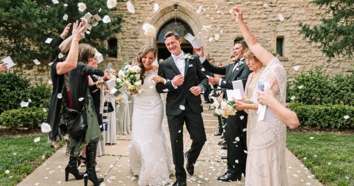 Bride and groom leaving a stone building while guests toss petals.